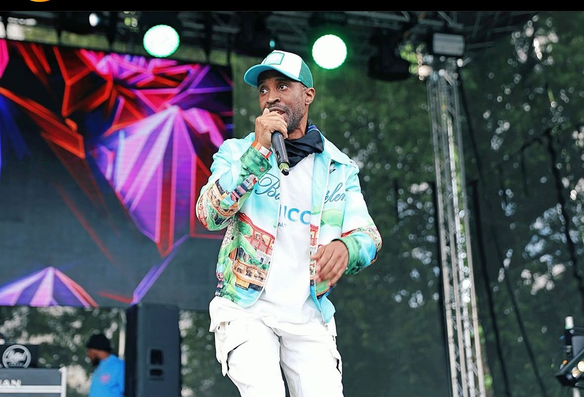 Raver performing on a festival main stage in a colourful jacket, microphone in hand
